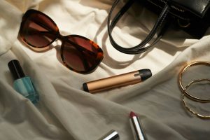 a pair of sunglasses, lipstick, and a purse on a bed